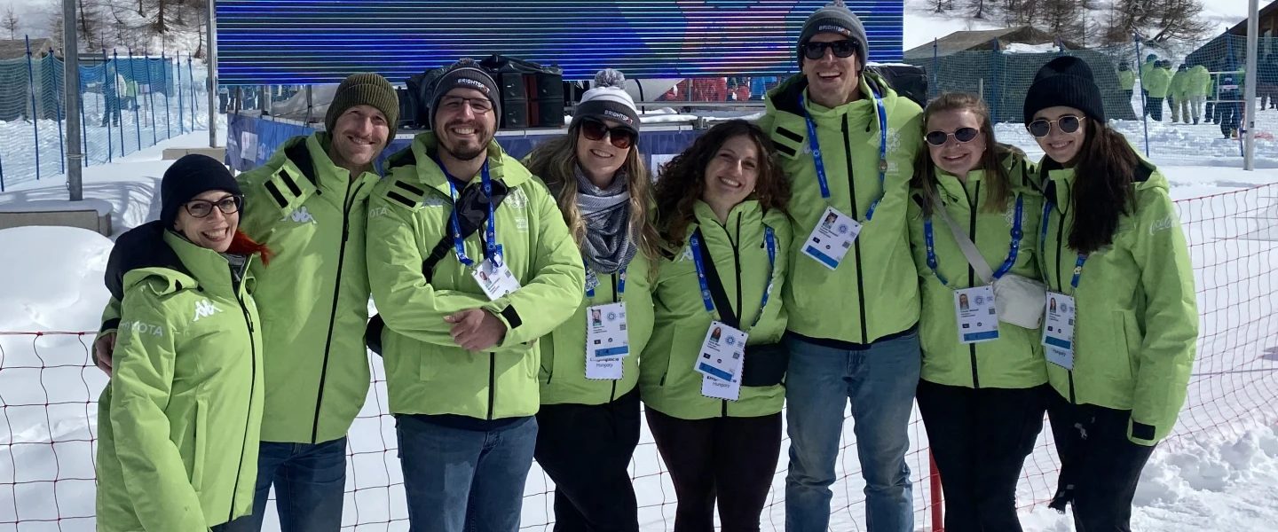 A team of eight Brightspot employee volunteers smiles together in front of snow-capped mountains in Turin, Italy, while supporting the 2025 Special Olympics World Games